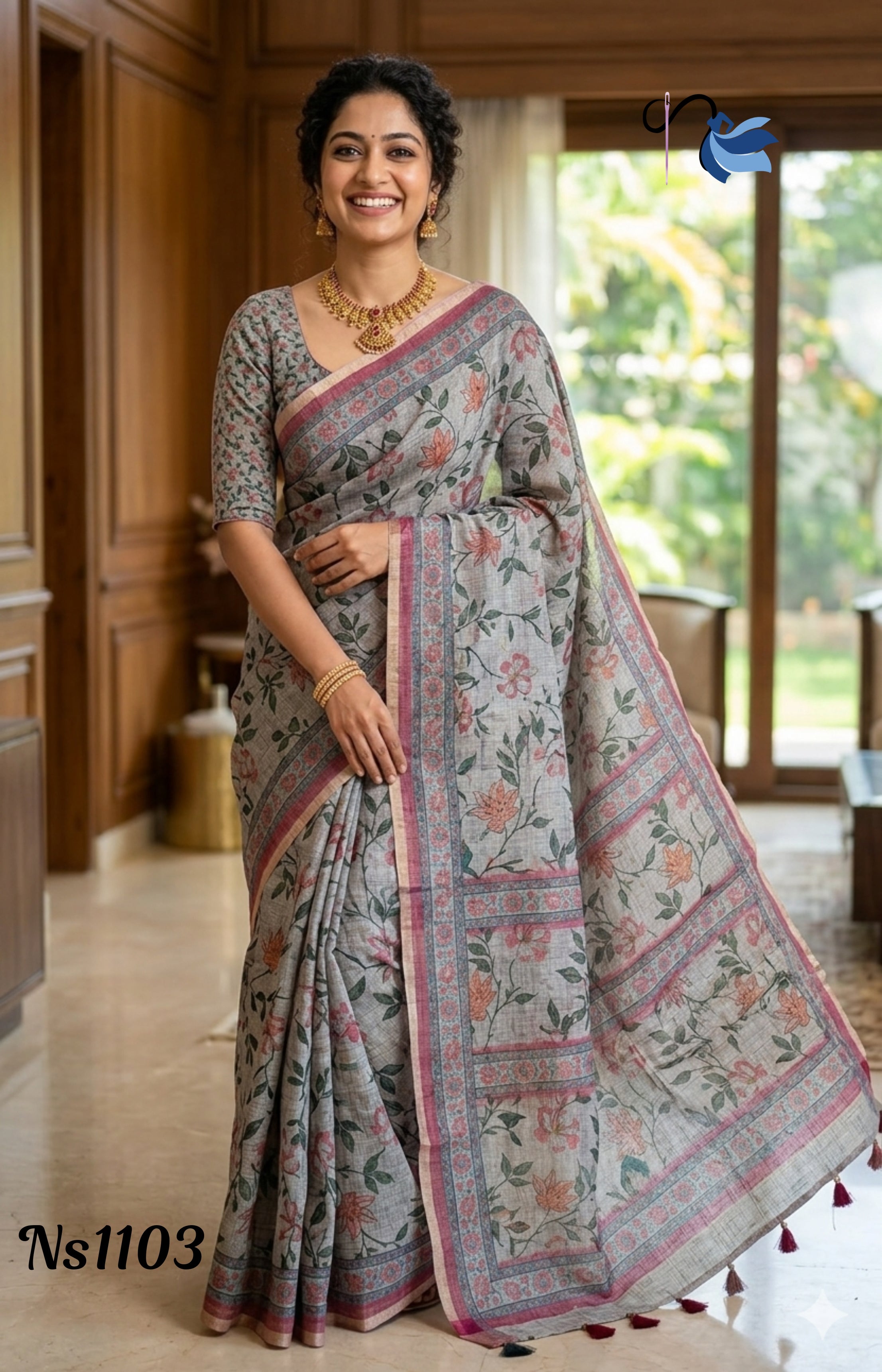 ​Woman in a silver grey linen saree with peach and coral floral vine prints and a pink zari border, accessorized with a gold temple necklace.
