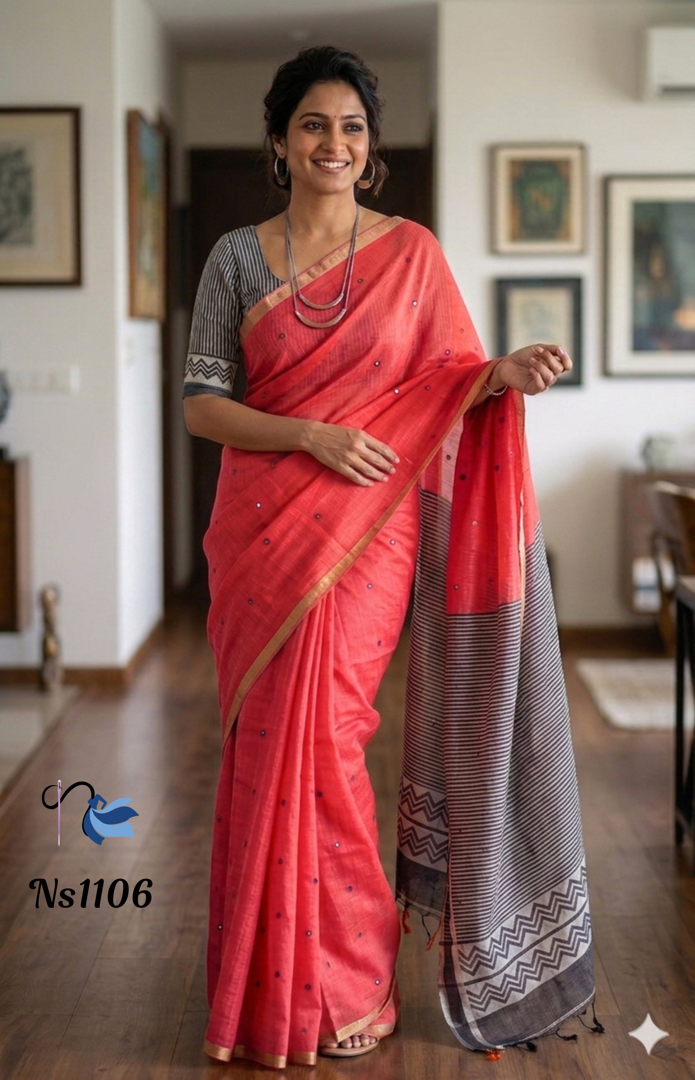 ​A woman smiling in a peach-coral linen cotton saree featuring tiny mirror-work details and a slim metallic border. She is wearing a grey and white striped blouse and layered oxidized silver jewelry. The saree is draped to showcase its contrasting grey pallu with horizontal stripes and geometric zigzag patterns.