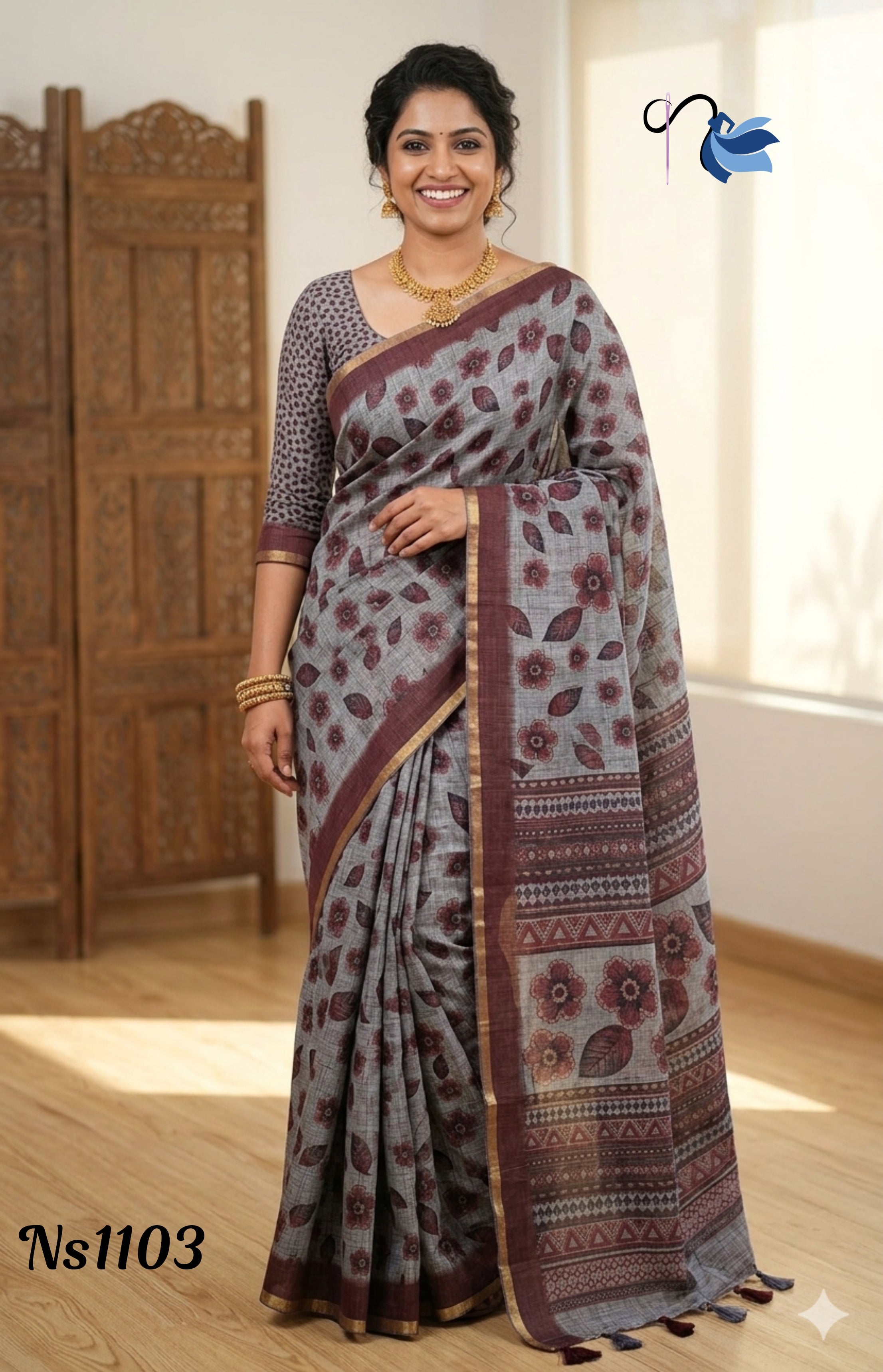 Woman smiling in an ash grey linen saree featuring maroon floral block prints and a patterned pallu, styled with a gold temple jewelry necklace and earrings.